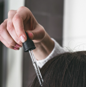 A hand applying a treatment serum from a glass dropper to dried hair.